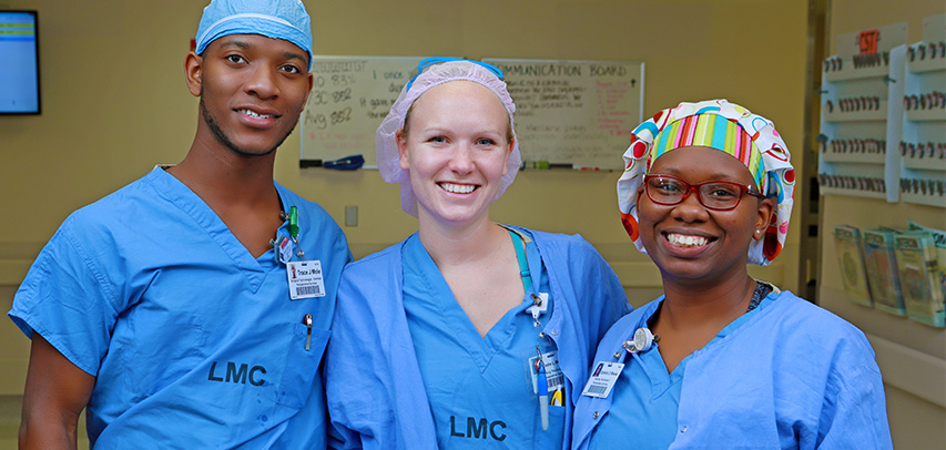 Three nurses smiling and wearing blue surgical scrubs that read LMC.