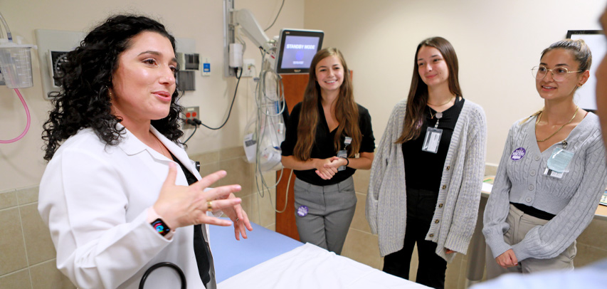 Dr. Kelli Hudon talking to a group of residents in a hospital room.