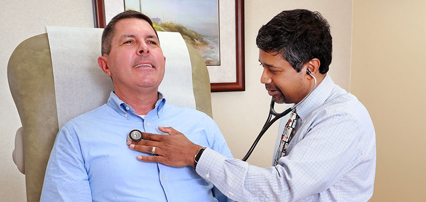 Keller Kissam, President of Dominion Energy, smiling as a doctor uses a stethoscope to listen to his heartbeat.