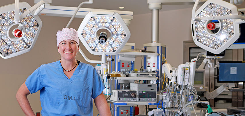 Dr. Heather Currier smiles for the camera in scrubs, hand on her hip, in a lab filled with impressive screening technology.