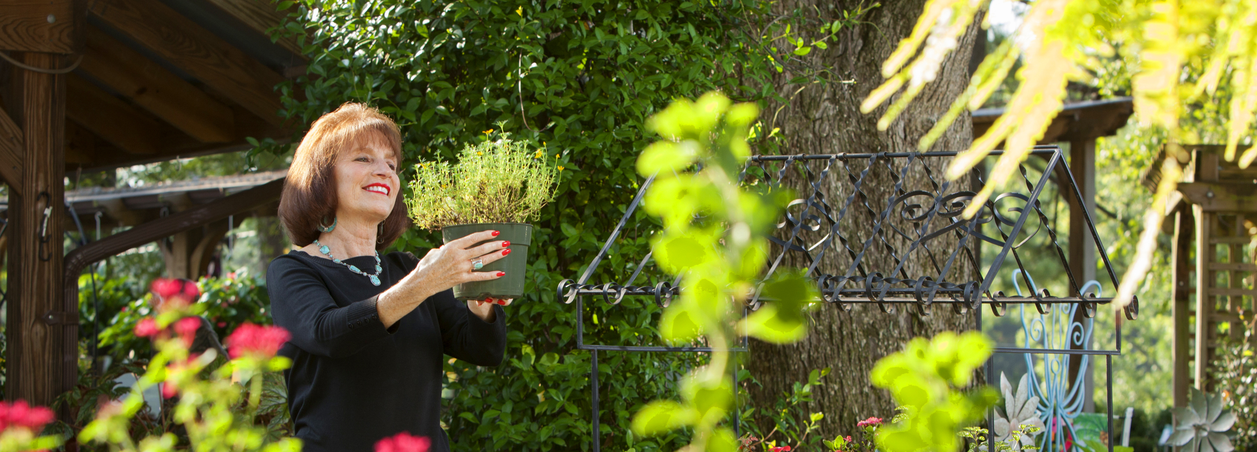 Heart patient Leslie Wyatt smiling as she gardens, holding up a potted plant in her sunlit yard.