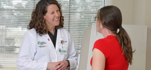 A female doctor in a white lab coat smiles warmly at a young patient in an exam room.