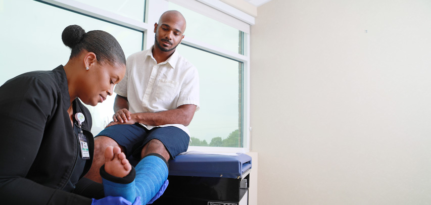 A medical technician checking a patient's leg in a cast.