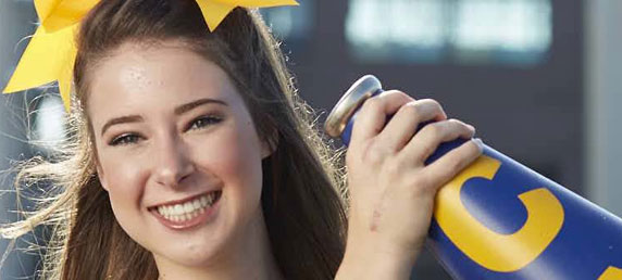 Hand injury patient Madison Kutyla in a cheer uniform holding up a megaphone on a football field.