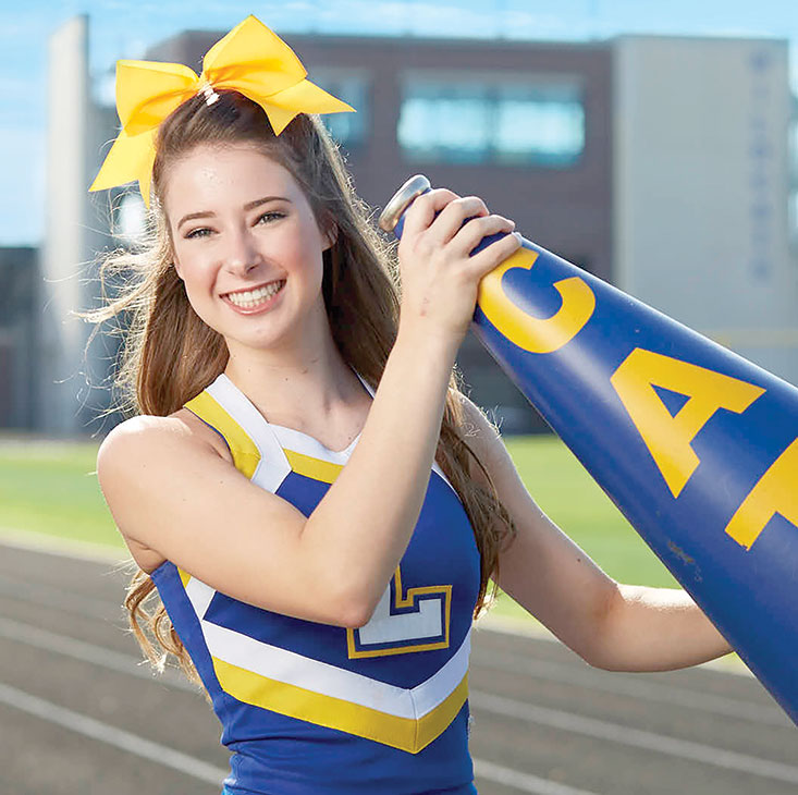 Hand injury patient Madison Kutyla in a cheer uniform holding up a megaphone on a football field.